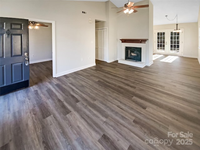 unfurnished living room featuring dark wood-type flooring, high vaulted ceiling, a brick fireplace, and french doors