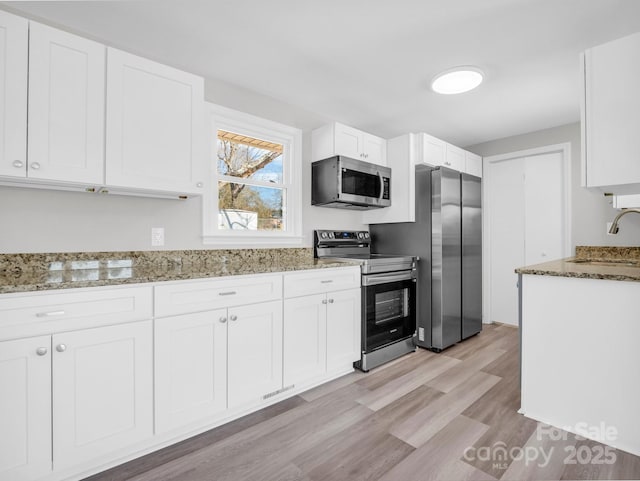 kitchen with sink, appliances with stainless steel finishes, white cabinetry, light hardwood / wood-style floors, and stone countertops