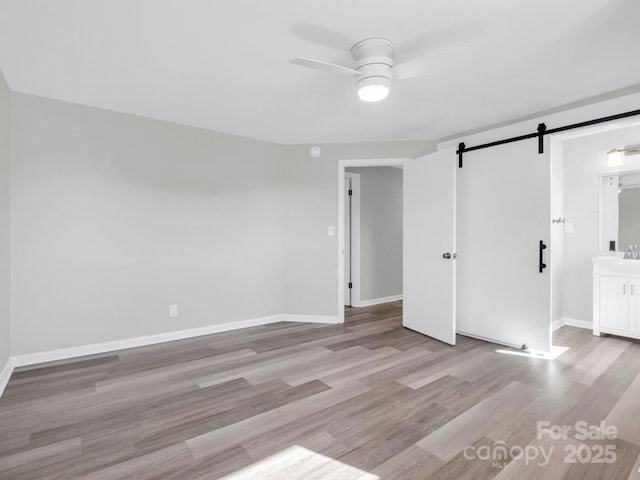 unfurnished bedroom featuring ceiling fan, a barn door, sink, and light hardwood / wood-style floors