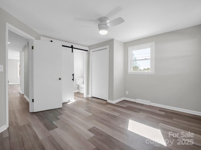 unfurnished room with light hardwood / wood-style flooring, a barn door, and ceiling fan