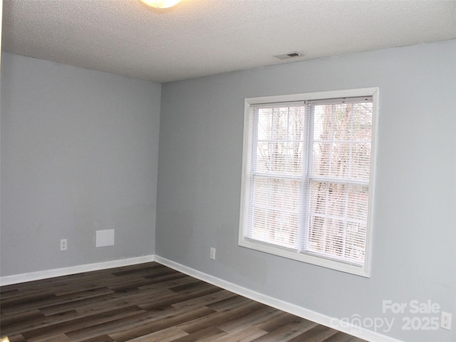 empty room with dark wood-type flooring, a wealth of natural light, and a textured ceiling