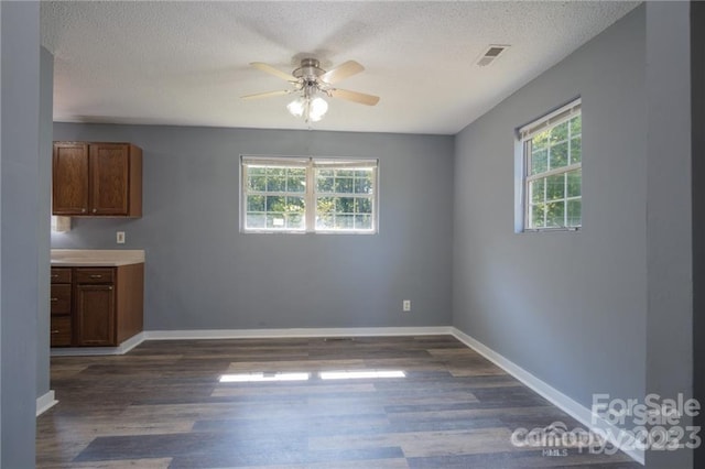 unfurnished dining area featuring ceiling fan, dark hardwood / wood-style floors, and a textured ceiling