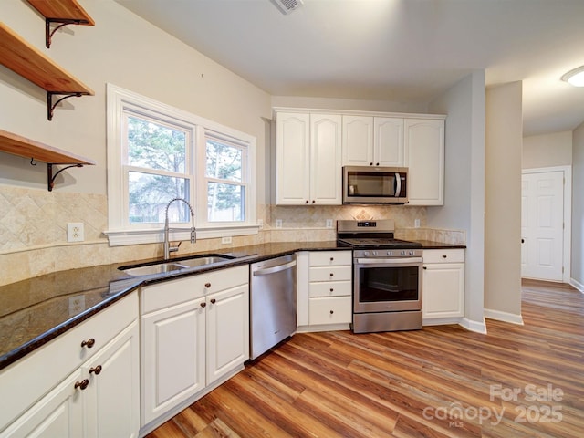 kitchen with stainless steel appliances, sink, white cabinets, and light hardwood / wood-style floors