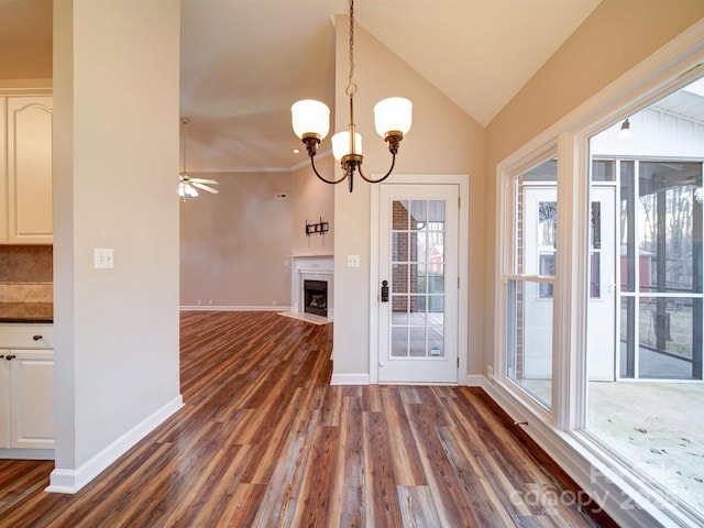 unfurnished dining area featuring lofted ceiling, dark wood-type flooring, plenty of natural light, and ceiling fan with notable chandelier