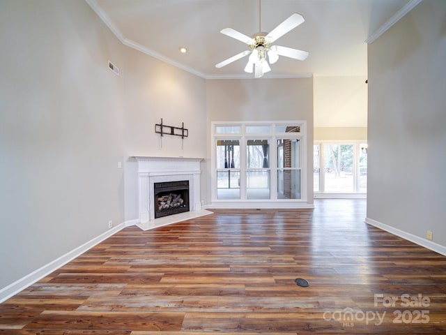 unfurnished living room featuring crown molding, ceiling fan, dark hardwood / wood-style floors, and a towering ceiling