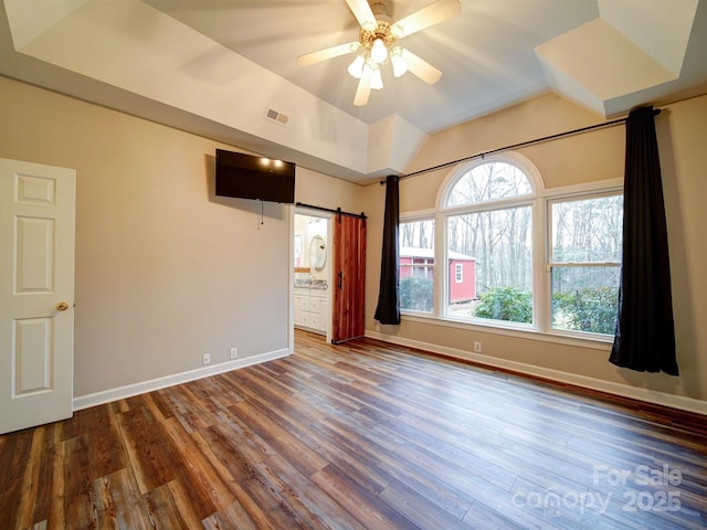 unfurnished bedroom with ensuite bathroom, wood-type flooring, lofted ceiling, ceiling fan, and a barn door