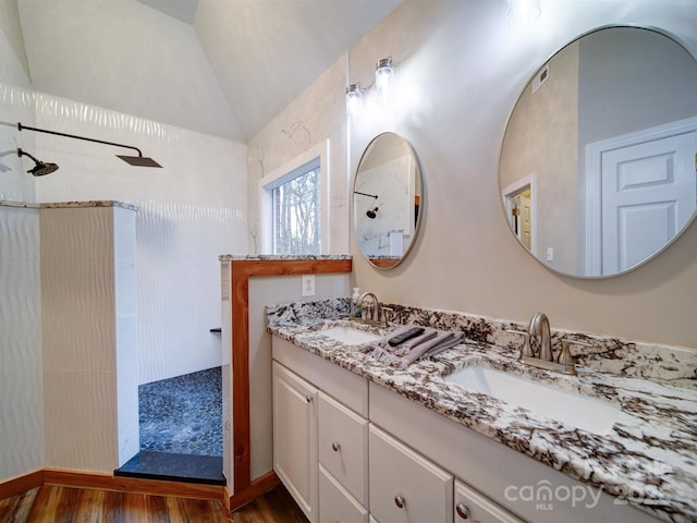 bathroom featuring tiled shower, lofted ceiling, wood-type flooring, and vanity