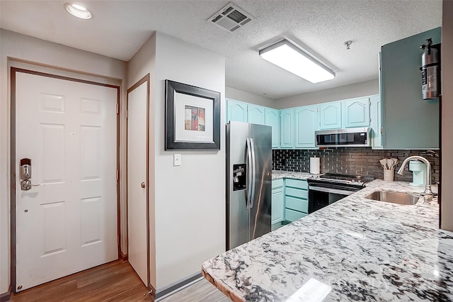 kitchen featuring appliances with stainless steel finishes, sink, light wood-type flooring, decorative backsplash, and a textured ceiling