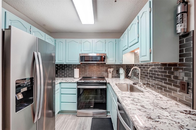 kitchen with blue cabinetry, sink, stainless steel appliances, light hardwood / wood-style floors, and decorative backsplash