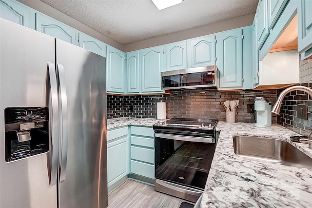 kitchen with appliances with stainless steel finishes, sink, decorative backsplash, blue cabinetry, and light wood-type flooring