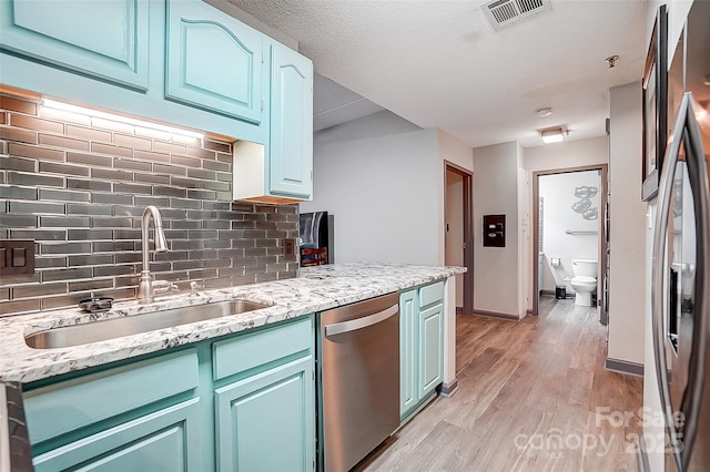 kitchen featuring appliances with stainless steel finishes, sink, decorative backsplash, light stone counters, and light wood-type flooring