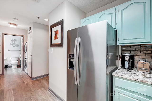 kitchen featuring blue cabinets, tasteful backsplash, stainless steel fridge with ice dispenser, stacked washing maching and dryer, and light hardwood / wood-style floors