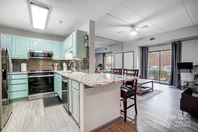 kitchen with sink, a kitchen bar, light hardwood / wood-style floors, kitchen peninsula, and stainless steel appliances