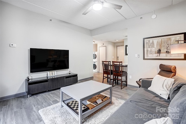 living room with stacked washer and dryer, wood-type flooring, and ceiling fan