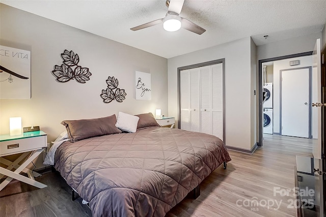 bedroom with stacked washer / dryer, a textured ceiling, light wood-type flooring, and a closet