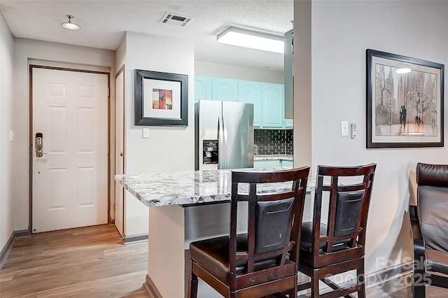 kitchen with stainless steel fridge with ice dispenser, a breakfast bar area, decorative backsplash, kitchen peninsula, and light wood-type flooring