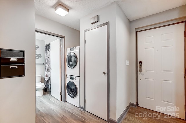 clothes washing area featuring stacked washer / drying machine, light hardwood / wood-style floors, and a textured ceiling