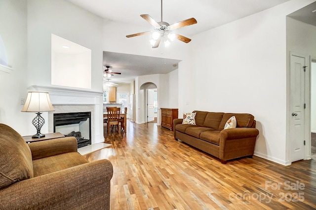 living room featuring a high ceiling, a multi sided fireplace, ceiling fan, and light wood-type flooring