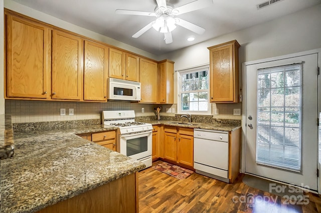 kitchen featuring sink, dark stone countertops, dark hardwood / wood-style floors, white appliances, and backsplash