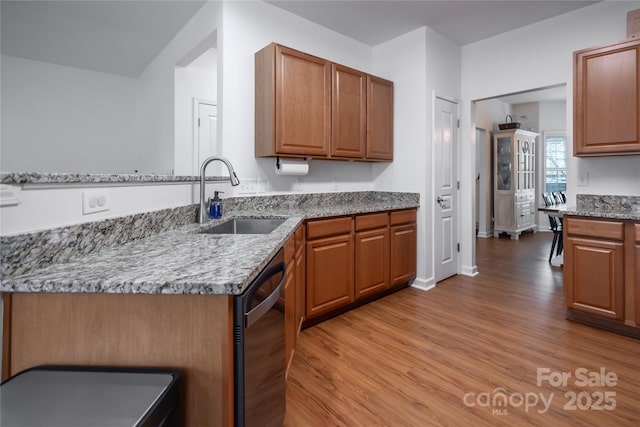 kitchen featuring sink, light hardwood / wood-style flooring, light stone countertops, and black dishwasher