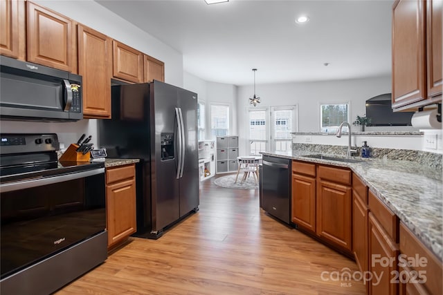 kitchen with sink, light stone counters, light hardwood / wood-style flooring, appliances with stainless steel finishes, and pendant lighting