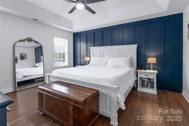 bedroom with ceiling fan, a tray ceiling, and dark hardwood / wood-style flooring