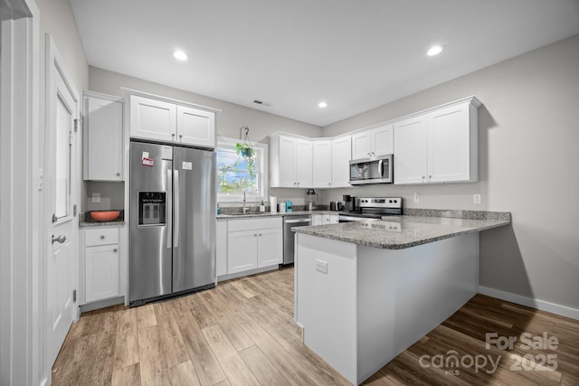 kitchen with sink, light hardwood / wood-style flooring, kitchen peninsula, stainless steel appliances, and white cabinets