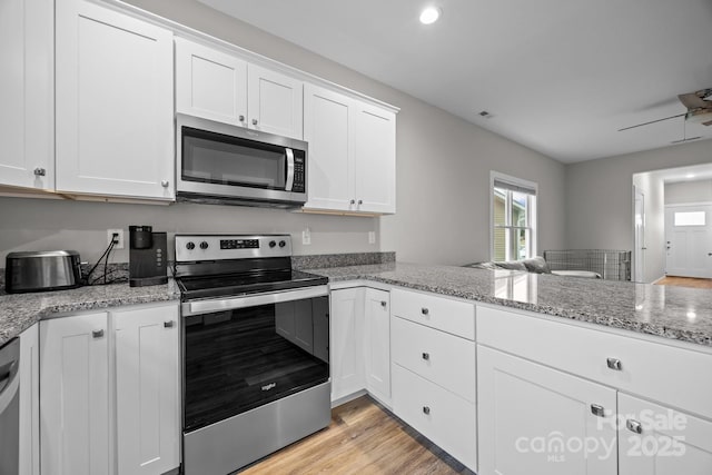 kitchen featuring light stone counters, light wood-type flooring, ceiling fan, stainless steel appliances, and white cabinets