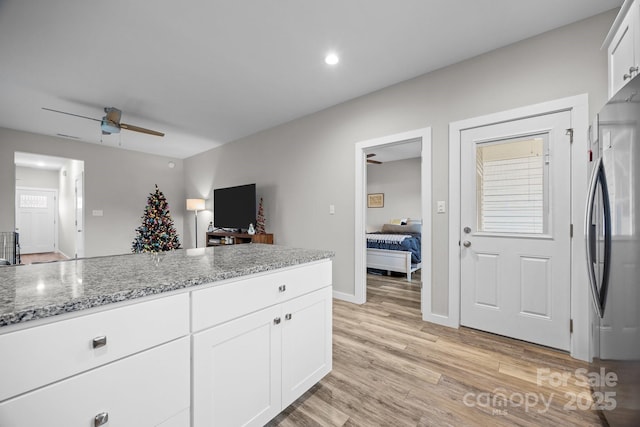 kitchen with stainless steel refrigerator, white cabinetry, ceiling fan, light stone counters, and light hardwood / wood-style floors