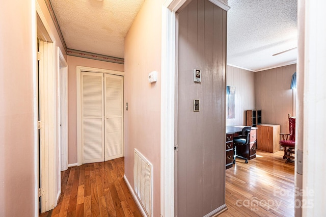 hallway featuring crown molding, hardwood / wood-style floors, and a textured ceiling