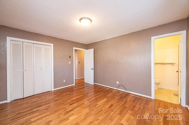 unfurnished bedroom with connected bathroom, hardwood / wood-style flooring, a closet, and a textured ceiling