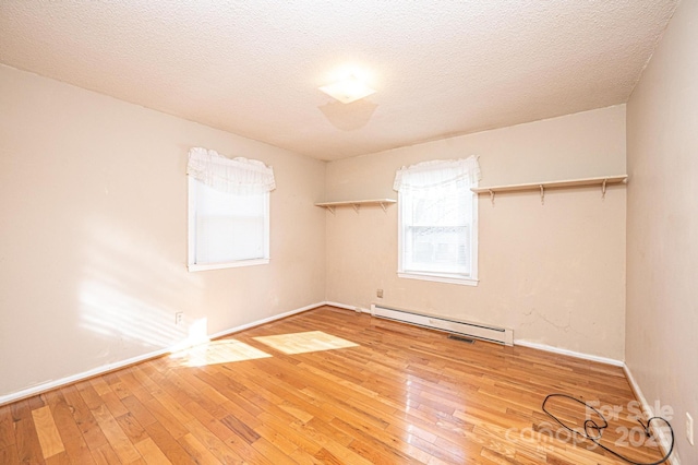 empty room featuring hardwood / wood-style flooring, a baseboard heating unit, and a textured ceiling