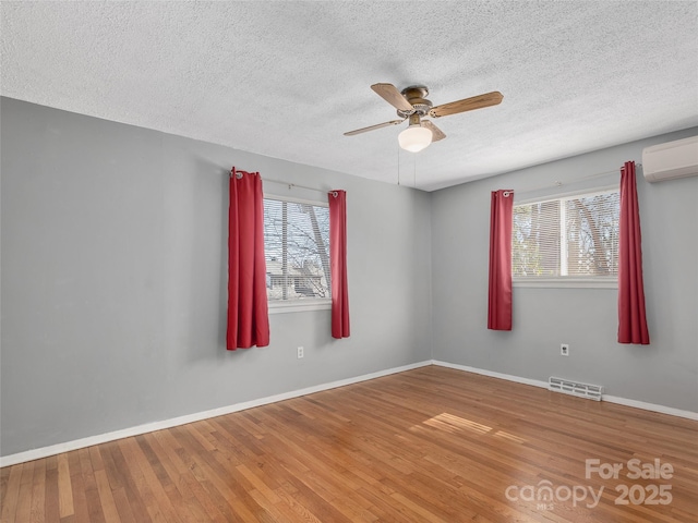 unfurnished room featuring an AC wall unit, a wealth of natural light, wood finished floors, and visible vents