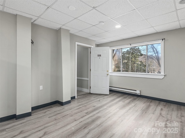 spare room featuring a baseboard heating unit, wood finished floors, and baseboards