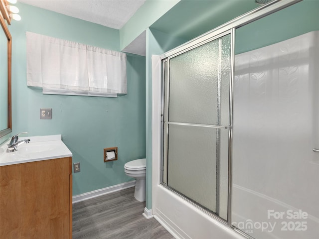bathroom with toilet, shower / bath combination with glass door, wood finished floors, vanity, and baseboards