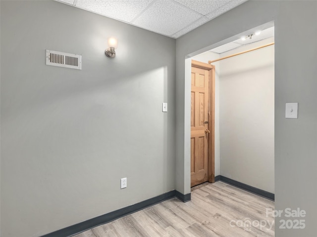 interior space featuring light wood finished floors, baseboards, visible vents, and a drop ceiling
