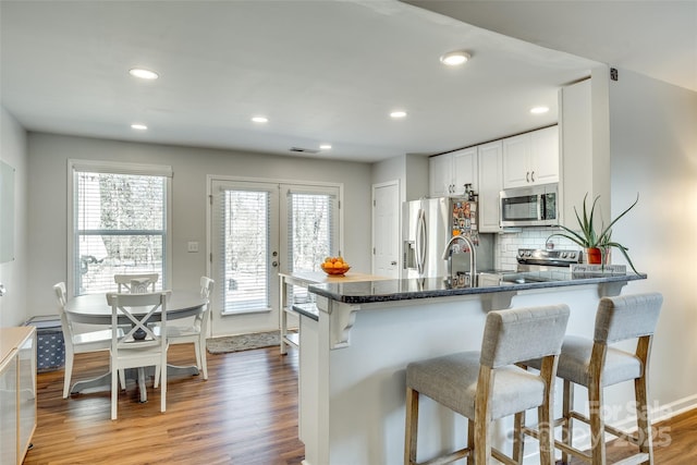 kitchen featuring white cabinetry, kitchen peninsula, stainless steel appliances, hardwood / wood-style floors, and decorative backsplash