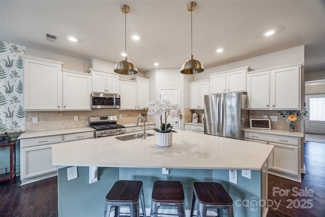 kitchen with sink, decorative light fixtures, stainless steel appliances, and a center island with sink