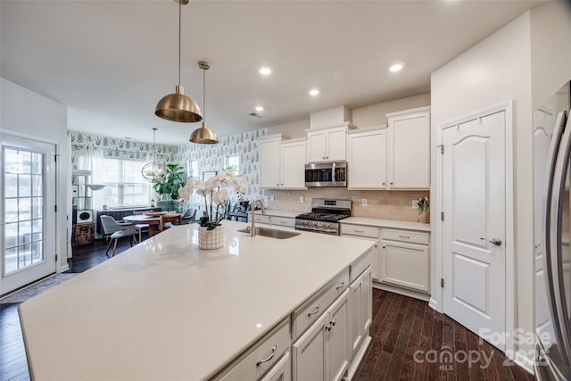 kitchen featuring sink, stainless steel appliances, an island with sink, white cabinets, and decorative light fixtures