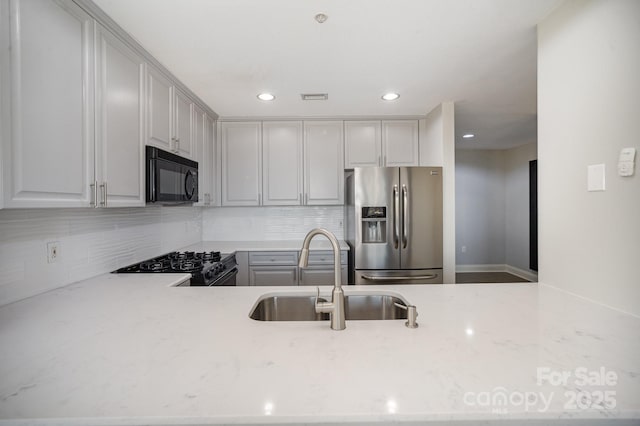 kitchen with sink, gray cabinetry, backsplash, black appliances, and light stone countertops