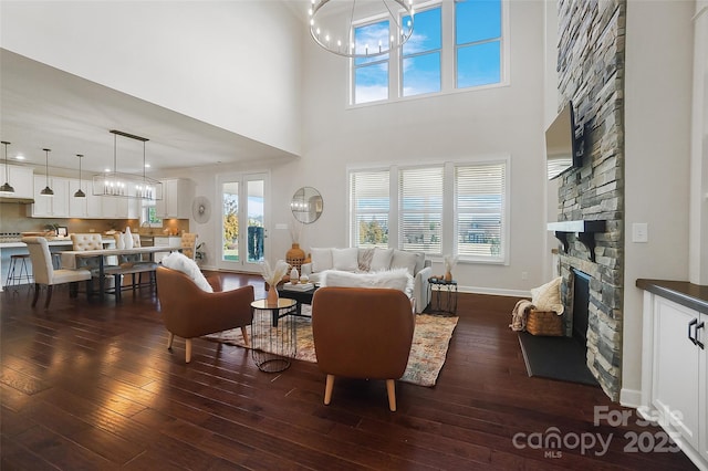 living room with dark hardwood / wood-style flooring, a towering ceiling, a notable chandelier, and a fireplace