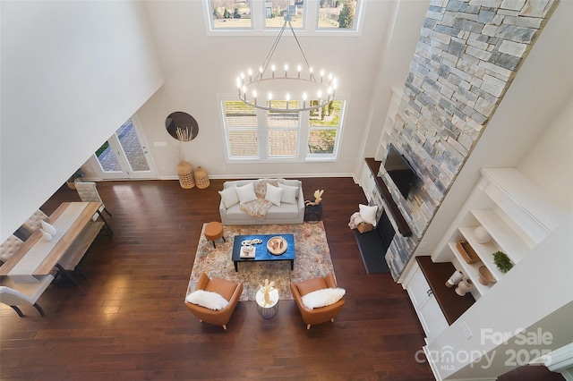 living room featuring a stone fireplace, dark hardwood / wood-style floors, a chandelier, and a towering ceiling