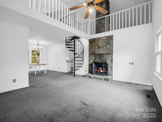 unfurnished living room with a stone fireplace, ceiling fan with notable chandelier, a high ceiling, and carpet flooring