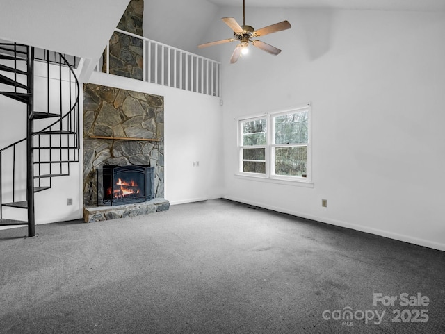 unfurnished living room with ceiling fan, a stone fireplace, carpet floors, and a high ceiling