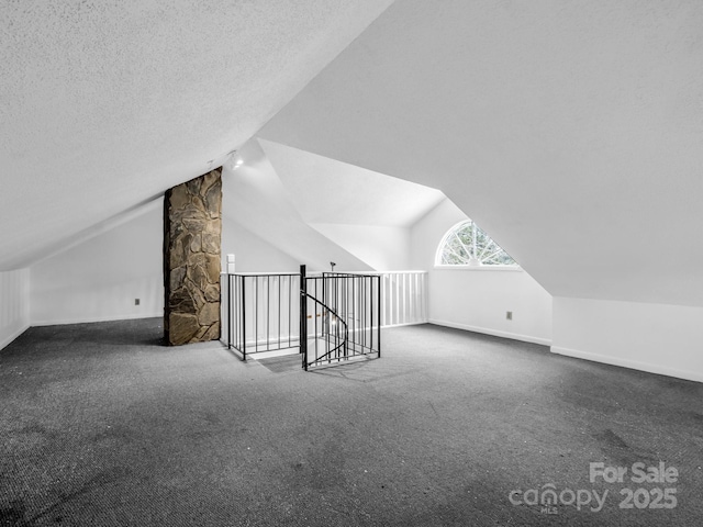 additional living space featuring vaulted ceiling, a textured ceiling, and dark colored carpet