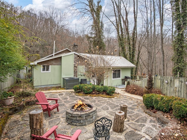 rear view of property featuring a patio, a chimney, central AC unit, fence, and a fire pit