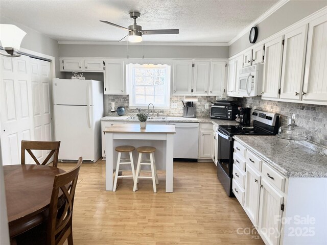 kitchen with a breakfast bar area, light countertops, light wood-style flooring, white appliances, and white cabinetry