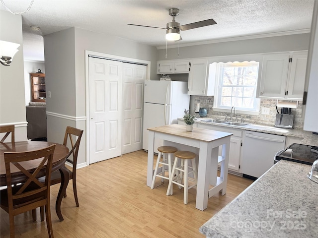 kitchen with light wood finished floors, white appliances, white cabinetry, and a sink