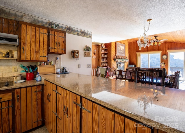 kitchen with pendant lighting, decorative backsplash, wooden walls, and a textured ceiling