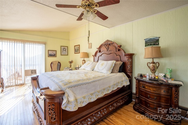 bedroom featuring vaulted ceiling, a textured ceiling, hardwood / wood-style flooring, ceiling fan, and access to exterior